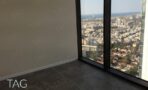 חדר עם חלון זכוכית גבוה ונוף לים ולעיר מקומה גבוהה, ריצוף אפור וקיר בהיר