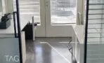 כניסה למשרד להשכרה בתל אביב עם רצפת בטון מוחלקת, שולחן לבן ומחיצת זכוכית במסגרת שחורה
