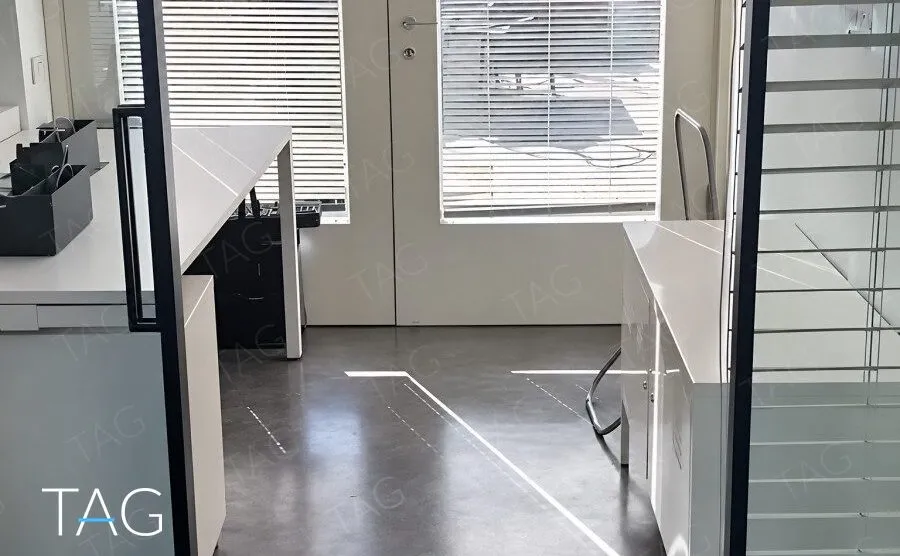 כניסה למשרד להשכרה בתל אביב עם רצפת בטון מוחלקת, שולחן לבן ומחיצת זכוכית במסגרת שחורה