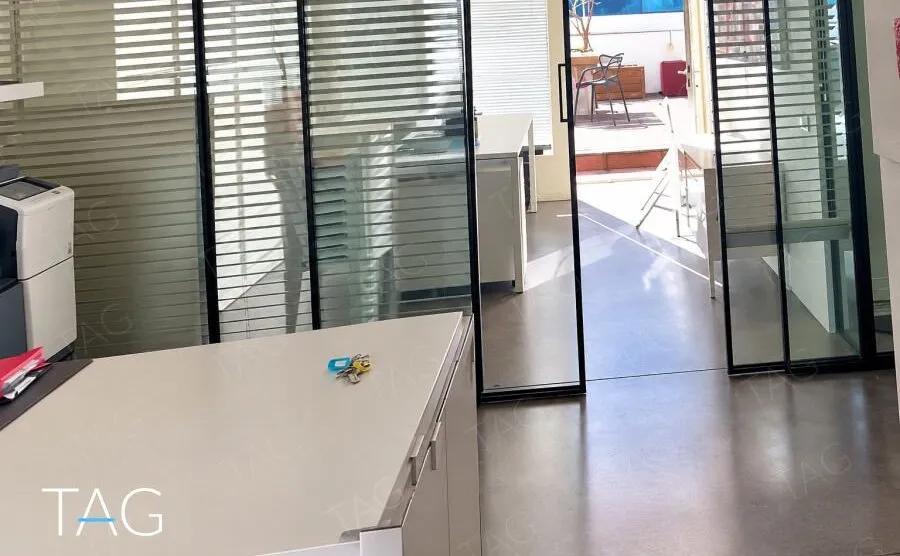 מחיצות זכוכית עם פסי הצללה ודלת הזזה שדרכה נראה הגג של המשרד להשכרה