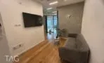 קבלה עם ספה אפורה, קיר בטון חשוף, טלוויזיה על הקיר וצמח בפינה במשרד להשכרה בבורסה