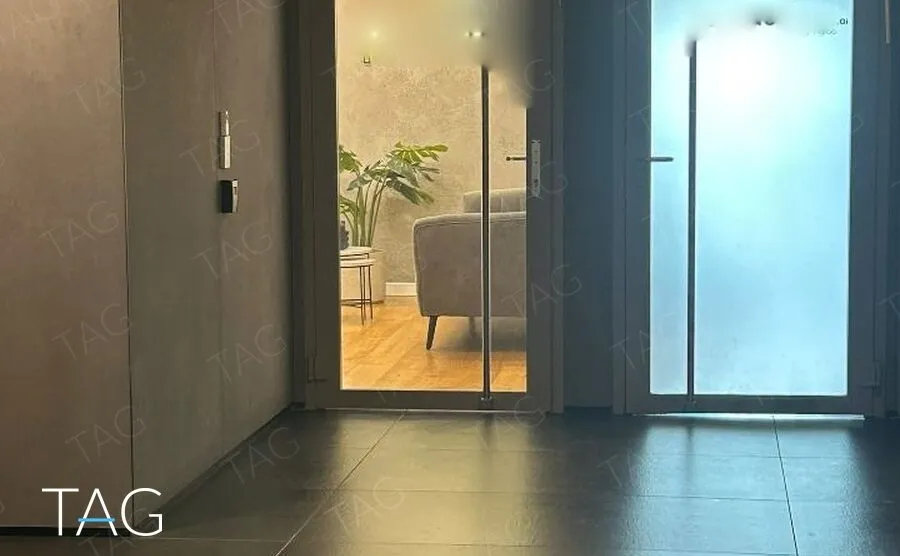 דלתות כניסה מזכוכית ממסגרת אפורה במסדרון הקומה, ומאחוריהן קבלה עם ספה ופרקט במגדל ספיר