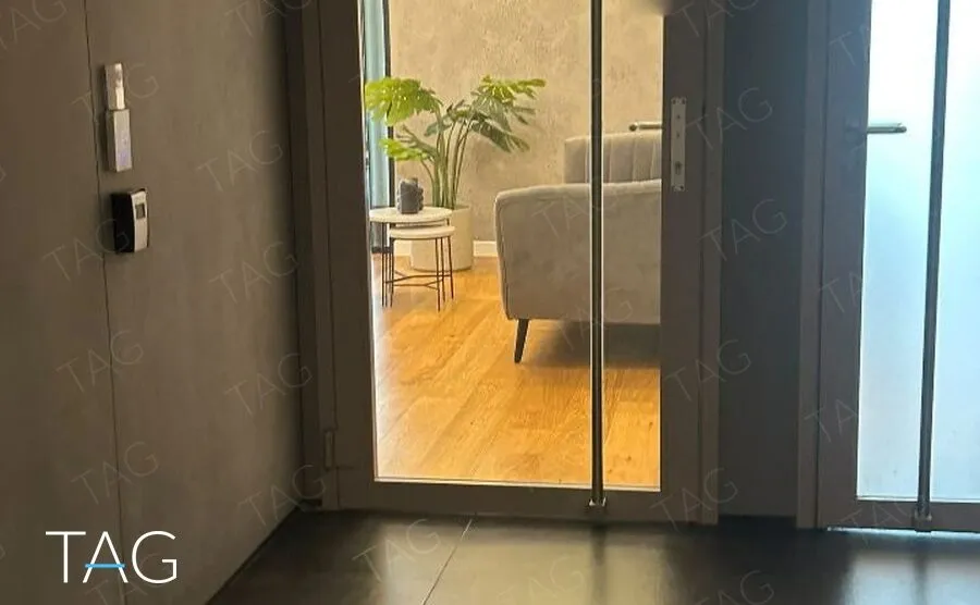 דלת כניסה זכוכית למשרד, ומבעדה פינת המתנה עם ספה אפורה, צמח ופרקט עץ ברמת גן