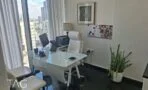 חדר עבודה עם שולחן זכוכית לבן וכיסא מנהלים ליד חלון גבוה עם נוף לעיר