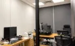 חדר עבודה עם שולחנות עץ וכיסאות ארגונומיים שחורים מאחורי מחיצת זכוכית, משרד להשכרה במגדל סקיי טאוור