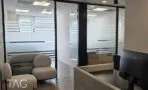 עמדת קבלה בגוון בטון ופינת המתנה עם כורסאות בהירות מול מחיצות זכוכית בפרופיל שחור, משרד להשכרה במגדלי אלון תל אביב