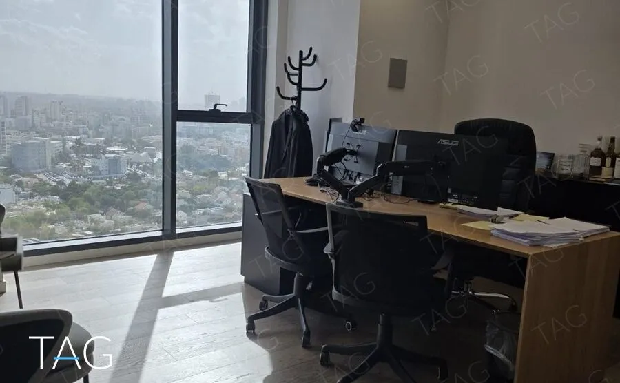 חדר מנהל עם שולחן עץ, כיסאות משרדיים וחלון מהרצפה עד התקרה עם נוף פתוח לתל אביב, מגדלי אלון
