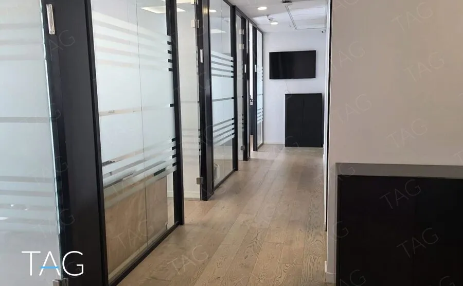 מסדרון עם פרקט עץ טבעי לאורך חדרים במחיצות זכוכית חלבית בפרופיל שחור, משרד במגדלי אלון