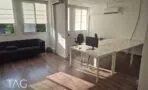 חלל עבודה פתוח ומואר עם עמדות לבנות, ספה כהה וחלונות בשני קירות