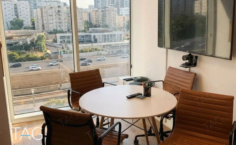 חדר ישיבות קטן עם שולחן עגול ונוף לעיר דרך חלון גבוה במשרד במגדל WE בתל אביב