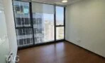 חדר משרד קטן עם חלון גבוה, תריס לבן ופרקט חום כהה, ובחוץ בנייני מגדלים ועגורני בנייה