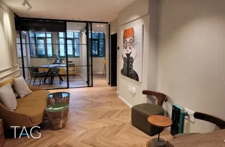 פינת המתנה עם ספה בצבע חרדל ופרקט פישבון מול חדר ישיבות במחיצות זכוכית, משרד להשכרה בשרונה תל אביב