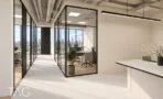 חדר מנהל בקיר זכוכית לצד מסדרון בהיר ודלפק לבן עם תאורה לינארית תלויה, תמונה להמחשה