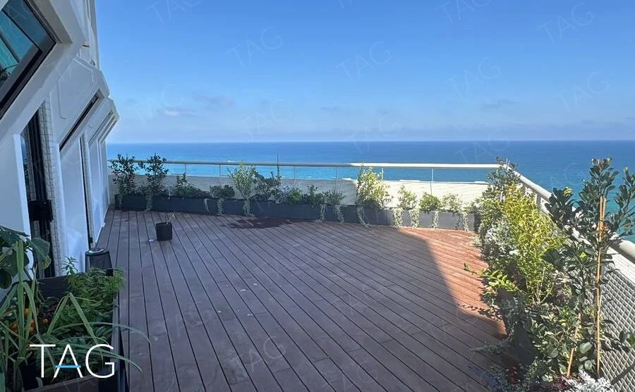 מרפסת דק עץ מרווחת עם ערוגות צמחייה ונוף פתוח לים התיכון במשרד להשכרה בבית הטקסטיל