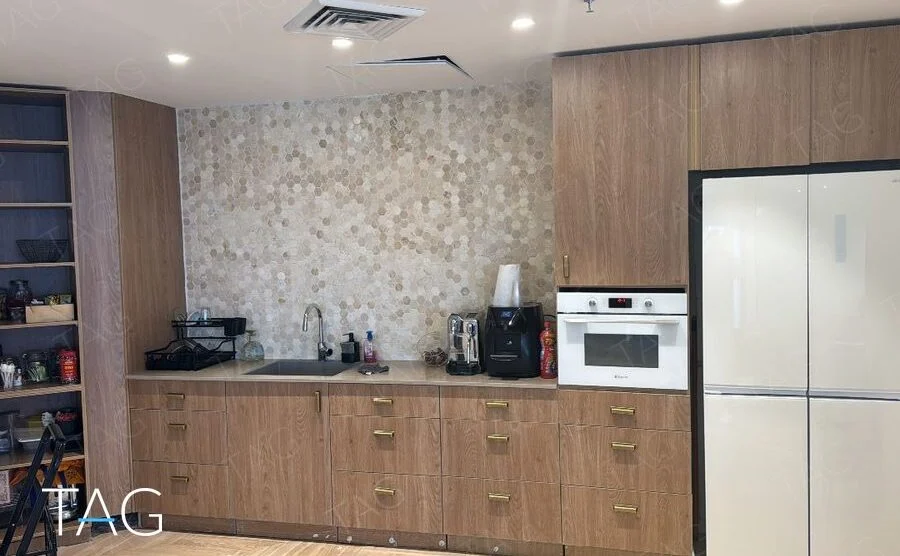מטבחון עם ארונות בגוון עץ, חיפוי פסיפס משושים, מקרר גדול ותנור משולב במשרד להשכרה בחוף הים