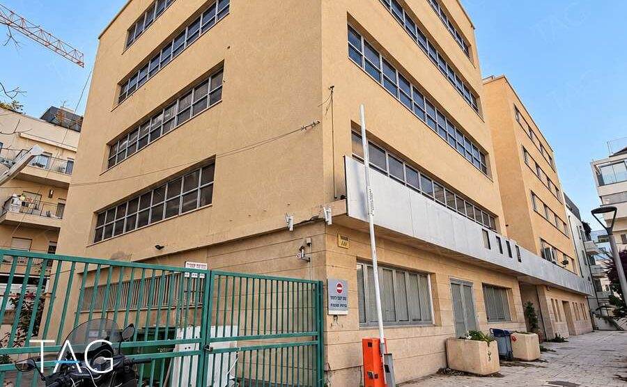 חזית בניין משרדים בגוון חול עם פסי חלונות אופקיים בסמטה להולכי רגל באזור רוטשילד בתל אביב