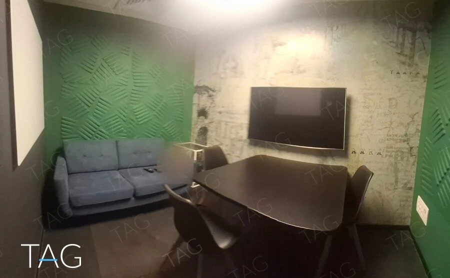 חדר צוות קטן עם קירות אקוסטיים ירוקים, ספה כחולה, שולחן ומסך