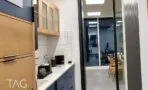 מטבחון עם משטח לבן ומכונת קפה, ופתח זכוכית לחדר עבודה מואר בלד