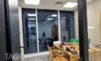 חדר עבודה עם שולחן עץ בהיר וכיסאות עץ, מבט דרך זכוכית לחדר סמוך, משרד 300 מ