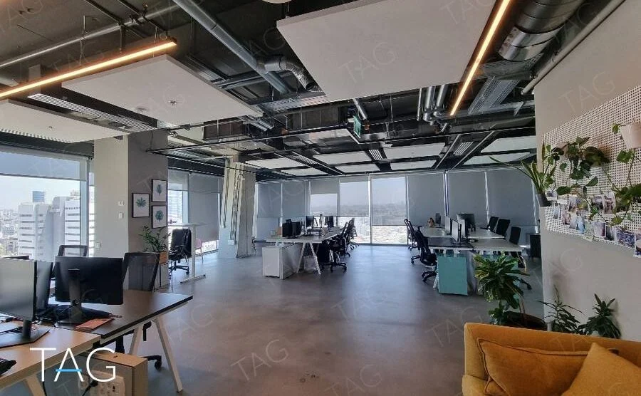אופן ספייס רחב עם תקרה חשופה, פאנלים אקוסטיים וספה צהובה במגדל רוטשילד 22