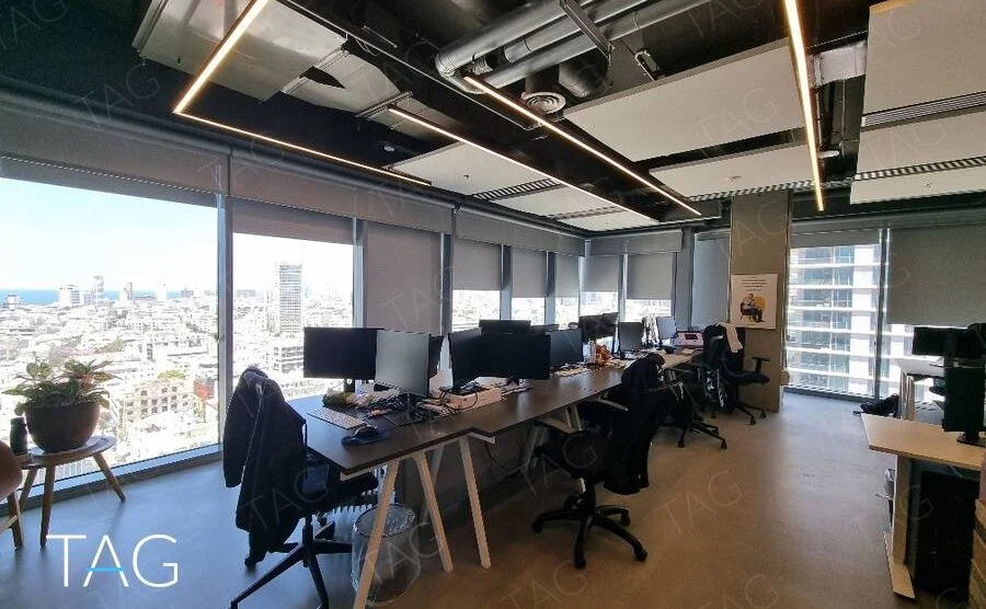 שורת עמדות עבודה לאורך חלונות עם וילונות גלילה ונוף לעיר ולים במשרד ברוטשילד
