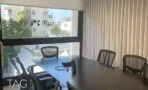 חדר ישיבות עם שולחן שחור, כיסאות רשת וחלון רחב אל הרחוב בתל אביב
