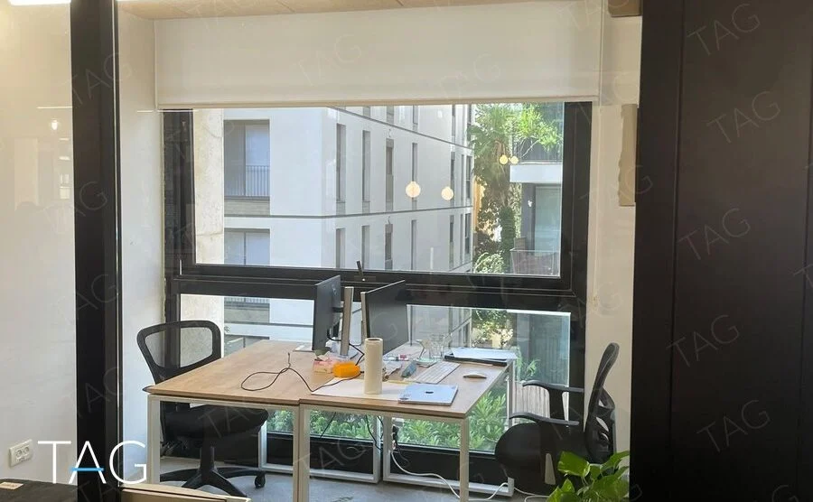 חדר עבודה קטן לשני אנשים עם שולחן עץ ורגליים לבנות מול חלון, עציץ ומחיצת זכוכית