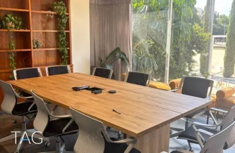 חדר ישיבות עם שולחן עץ מלא, כיסאות לבנים וחלון מקיר לקיר לעצים, משרד להשכרה ליד כיכר הבימה בתל אביב