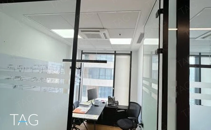 חדר עבודה סגור במחיצת זכוכית שחורה עם פסי חלבית, רצפת עץ בהירה ושולחן מול חלון במגדל רסיטל
