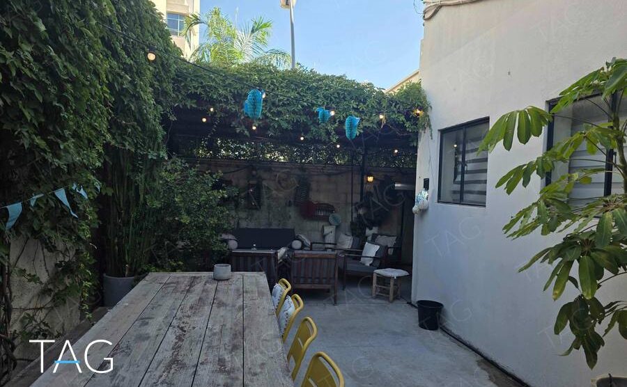 חצר צמודה למשרד בתל אביב עם פרגולה מכוסה צמחייה, שולחן עץ ארוך ופינת ישיבה
